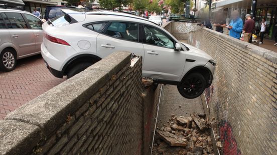 Auto rijdt dwars door muur, voorkant zweeft boven voetgangerstunnel